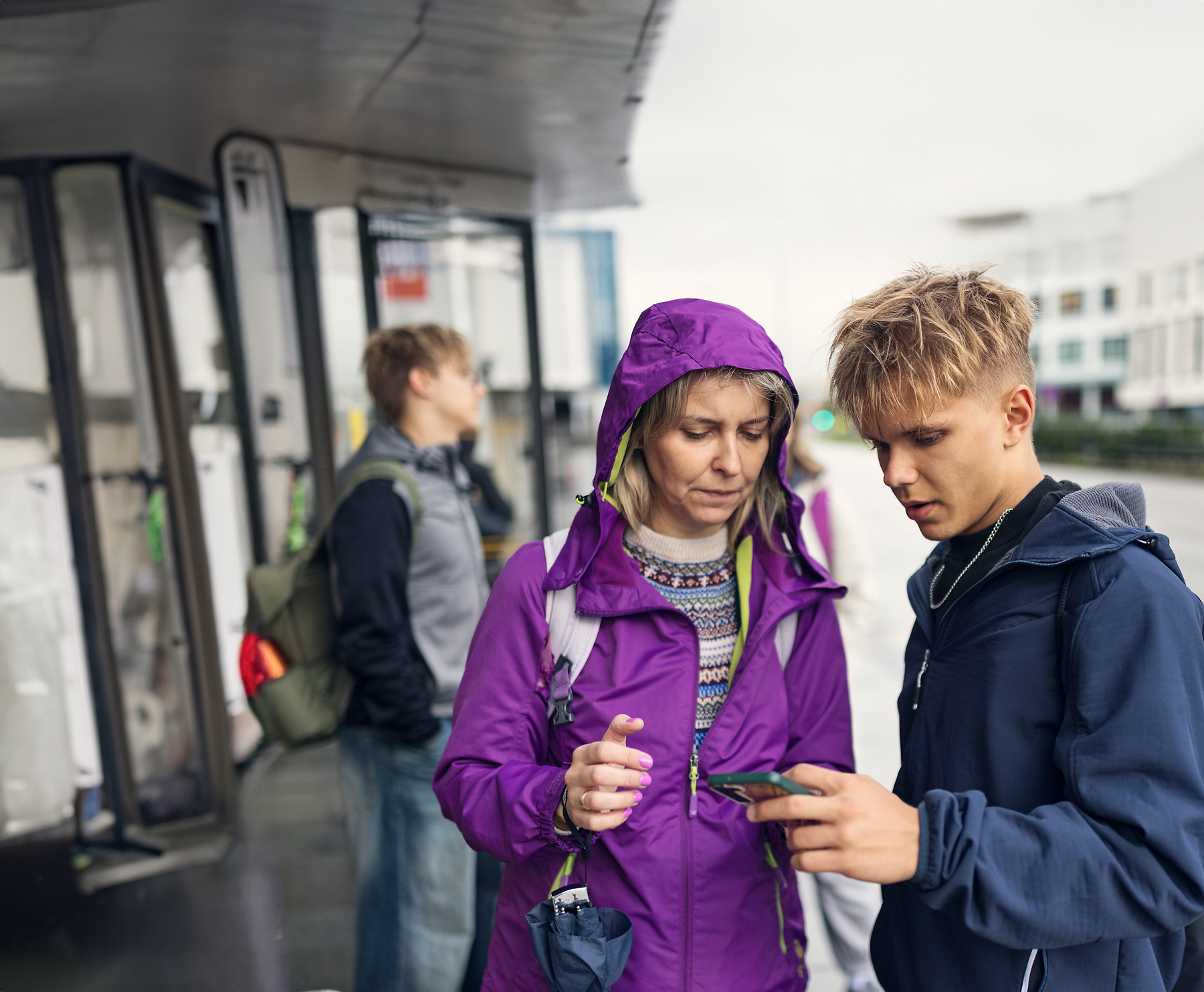 Mor och son kollar i en telefon i en busskur